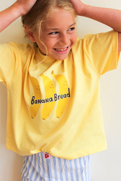 Child wearing a yellow 'Banana Bread' t-shirt with banana graphics against a plain background