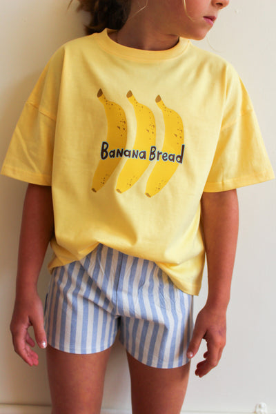 Person wearing a yellow t-shirt with banana graphics and 'Banana Bread' text, paired with blue and white striped shorts.