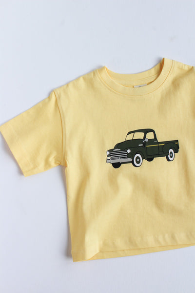 Yellow t-shirt with a green truck graphic on a light gray background