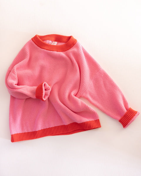 Pink knit sweater with red trim on a light beige background