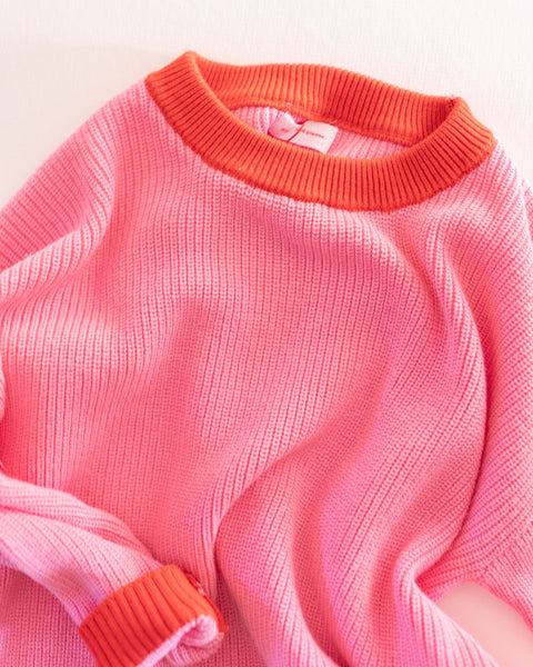 Pink knit sweater with red collar and cuffs on a white background