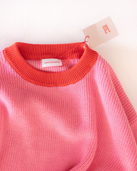 Pink knit sweater with red collar and a tag on a light background