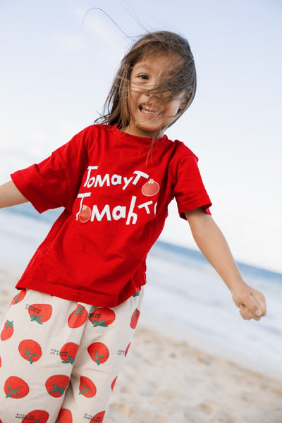 Child wearing a red shirt with graphic and white pants with red patterns on a beach.