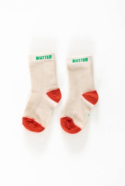 A pair of beige socks with the word 'BUTTER' printed in green on the top, designed for kids.