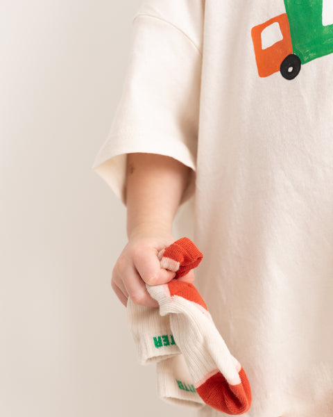 A pair of beige socks with the word 'BUTTER' printed in green on the top, designed for kids.