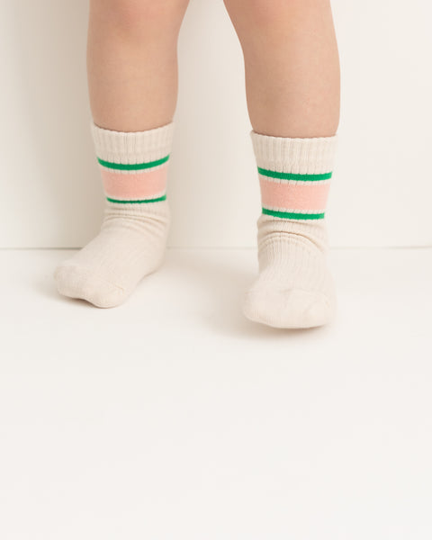A pair of socks with horizontal watermelon stripe patterns in pink and green colors on a beige background.