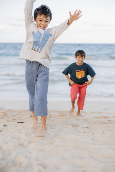 Two children wearing long sleeve t-shirts playing on a beach with ocean in the background