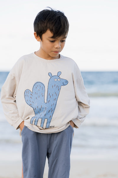 Child wearing a beige sweatshirt with a blue Camel design on a beach.