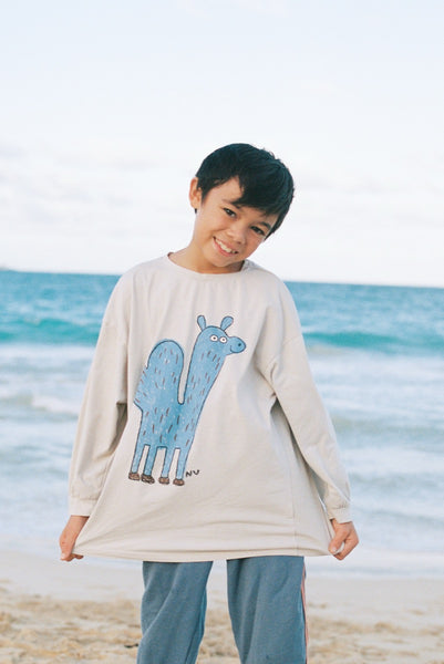Child wearing a long-sleeve shirt with a blue camel design on a beach