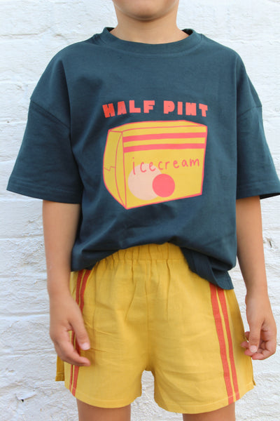 Child wearing a dark blue t-shirt with a half pint ice cream graphic and yellow shorts against a light wooden background