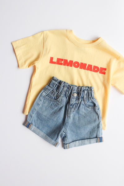 Yellow t-shirt with 'LEMONADE' text and denim shorts on a light gray background