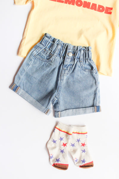 Yellow t-shirt with 'LEMONADE' text, blue denim shorts, and colorful star-patterned socks on a white background.