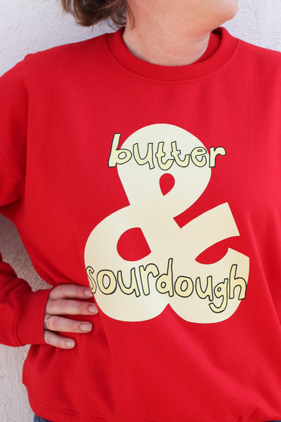 A closer shot of a Women wearing red cotton sweatshirt with a hand-drawn sourdough and butter graphic 