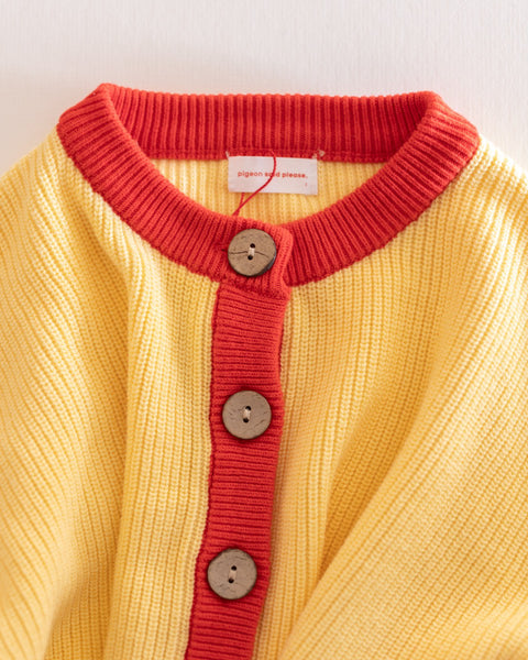 Yellow cardigan with red ribbed collar and buttons on a white background