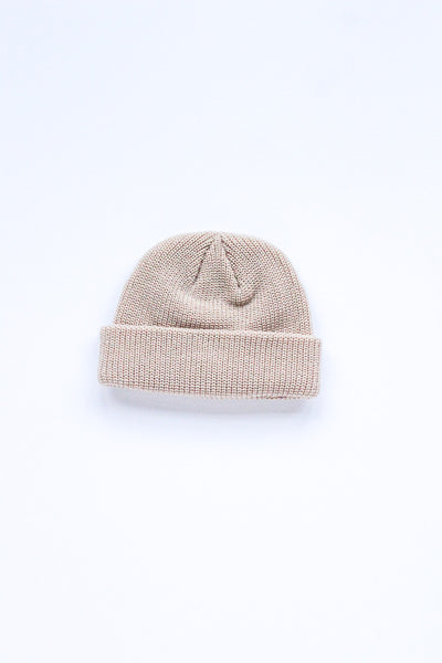 A light beige knit beanie hat with a folded cuff, photographed flat against a clean white background.