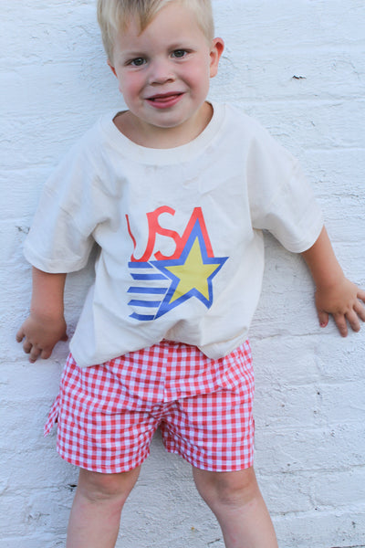 Child wearing a 'USA' t-shirt with a star graphic against a white brick wall.