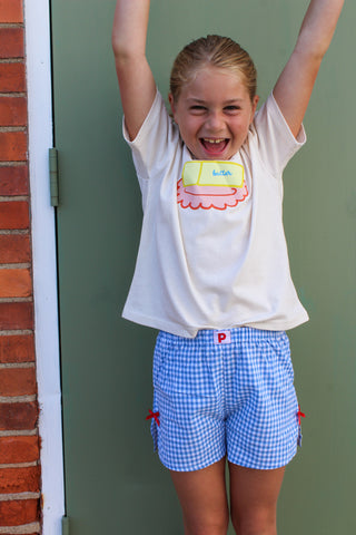 cream butter dish  t-shirt with a colorful design and blue checkered gingham shorts with red bow on side. 