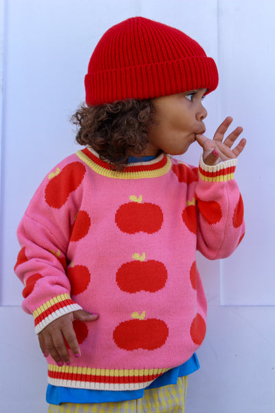 Child wearing apple sweater with a red beanie 