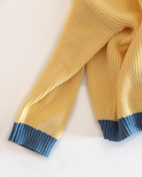 Yellow knit sweater with blue cuffs on a light background