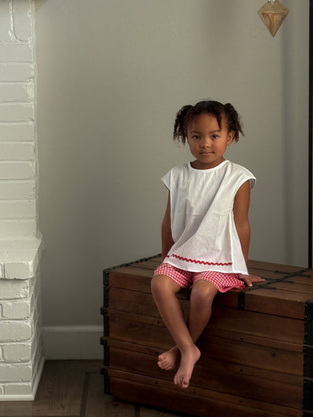 white tulip children's top with a red  strawberry button and red  gingham checkered shorts.