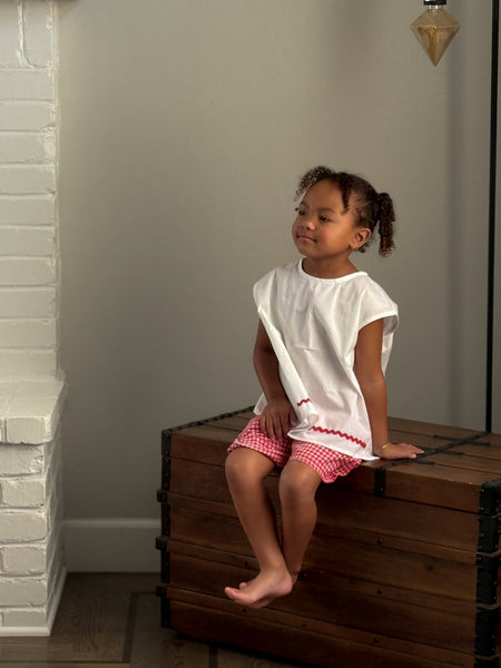 white tulip children's top with a red  strawberry button and red  gingham checkered shorts.