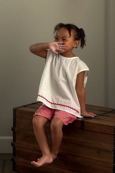white tulip children's top with a red  strawberry button and red  gingham checkered shorts.