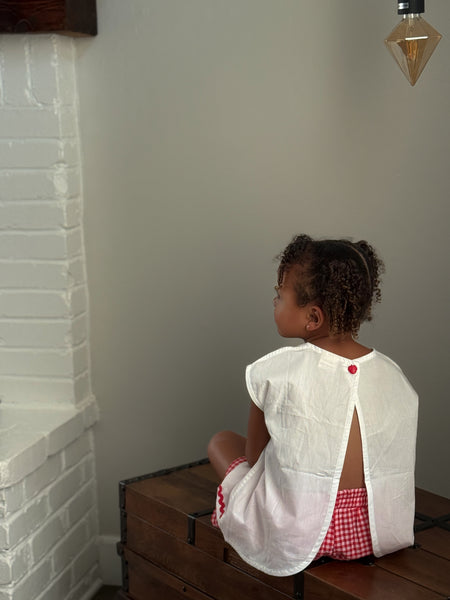 white tulip children's top with a red  strawberry button and red  gingham checkered shorts.