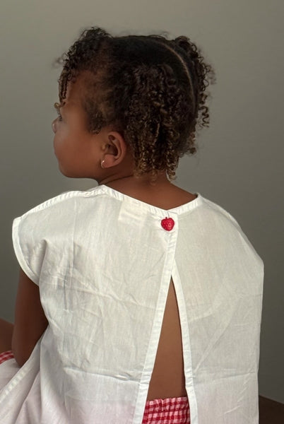 child wearing white tulip top with open back and strawberry button detail 