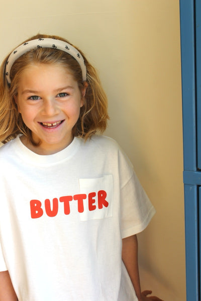 A smiling child wearing a beige headband with a ribbon print.