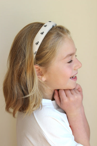 A smiling child wearing a beige headband with a ribbon print.