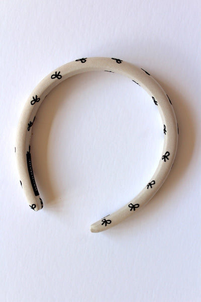 A beige headband with a small ribbon print, displayed against a white background.