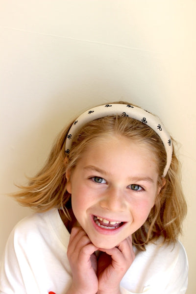 A smiling child wearing a beige headband with a ribbon print.