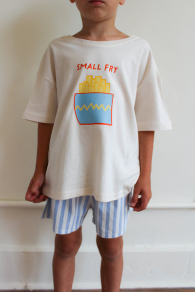 Child wearing a white t-shirt with a graphic design and striped shorts against a plain background