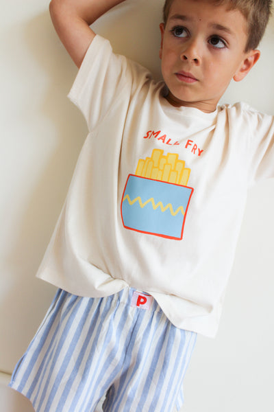 Child wearing a white t-shirt with a colorful graphic and striped shorts on a plain background