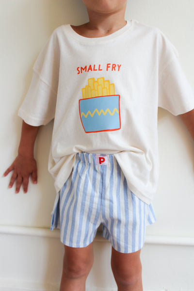 Child wearing a white t-shirt with a graphic design and blue striped shorts on a plain background