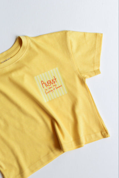 Yellow t-shirt that says "august is like the sunday of summer" on a white background