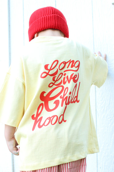 Child wearing yellow cotton t-shirt with hand-drawn orange childhood doodles on front and Long live childhood graphic on back
