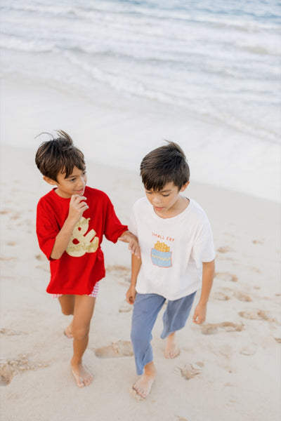 Two children on a beach wearing red and white t-shirts with graphic designs.