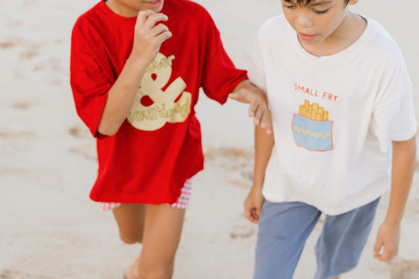 Two children on a beach wearing red and white t-shirts with graphic designs.