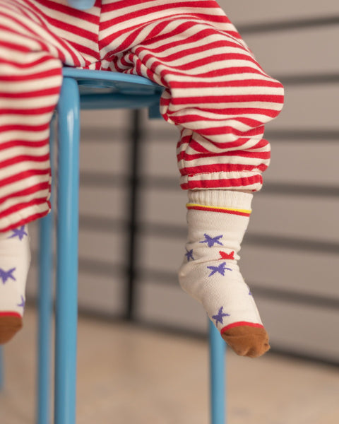Child wearing red and white striped pants and star-patterned socks sitting on a blue stool.