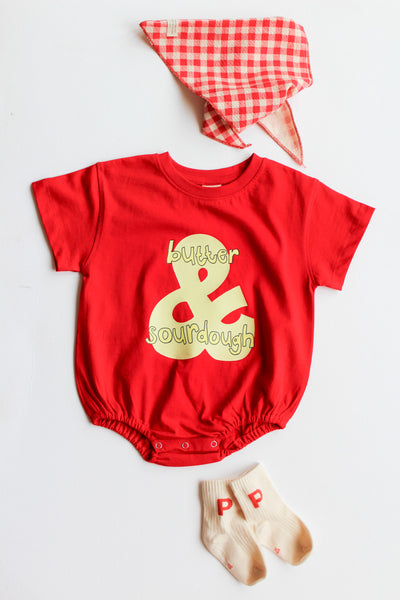 Red baby romper with butter & sourdough graphic matched with a red checkered bandana, and beige socks on a light gray background