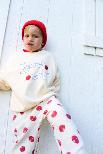 Kid wearing our cream cotton muslin pants with red tomato print and elastic waist and our Tomayto Tomahto cream sweatshirt and red beanie 