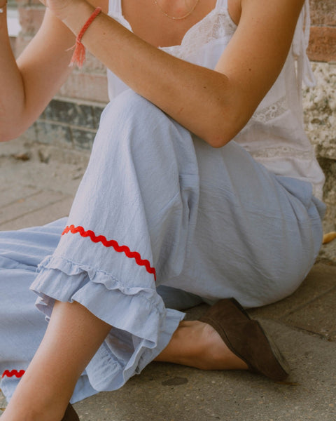 Person wearing a light blue pant with red trim sitting on a stone surface.