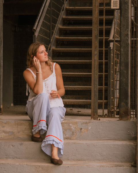 Woman sitting on a staircase wearing wide leg ruffle pant with red trim 