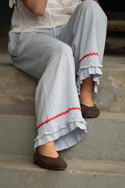 Person wearing light blue pants with red trim and brown shoes sitting on steps.