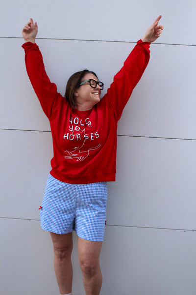 Person wearing a red sweatshirt with text and graphics, standing against a light-colored wall.