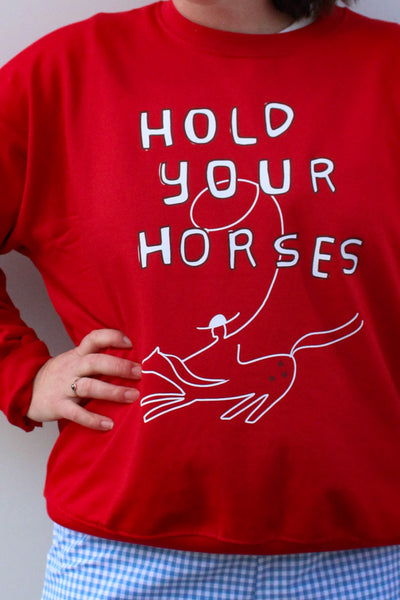 Red sweatshirt with 'Hold Your Horses' text and graphic, worn by a person.