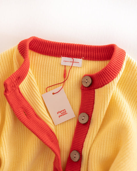 Yellow cardigan with red trim and buttons on a white background