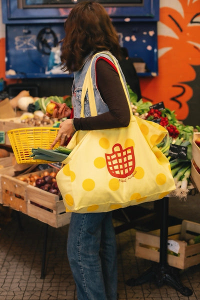 A person shopping for groceries using a yellow tote bag with a geometric pattern.